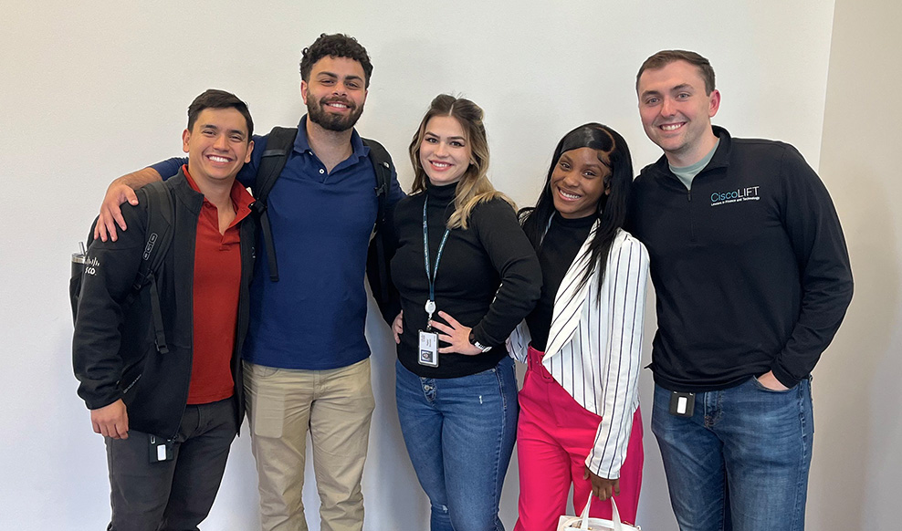 Five people stand together smiling.