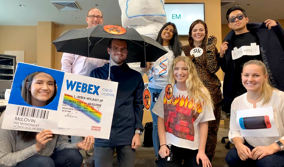 Group of eight people smiling. One holds an umbrella.