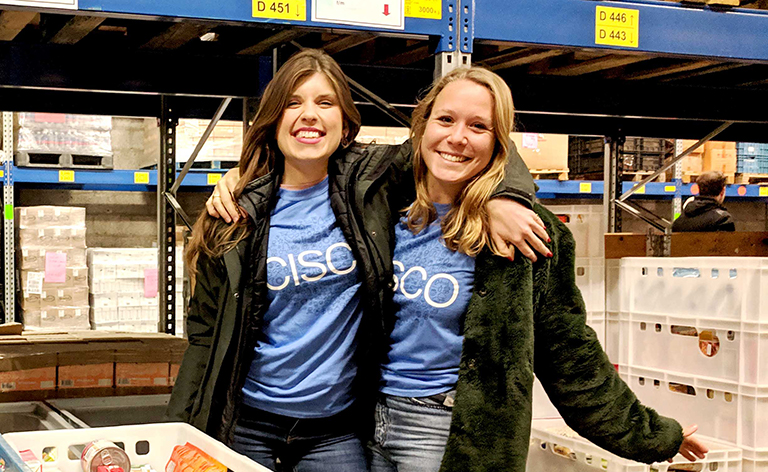 Two females wearing the same blue Cisco shirt volunteering at a food bank sorting produce