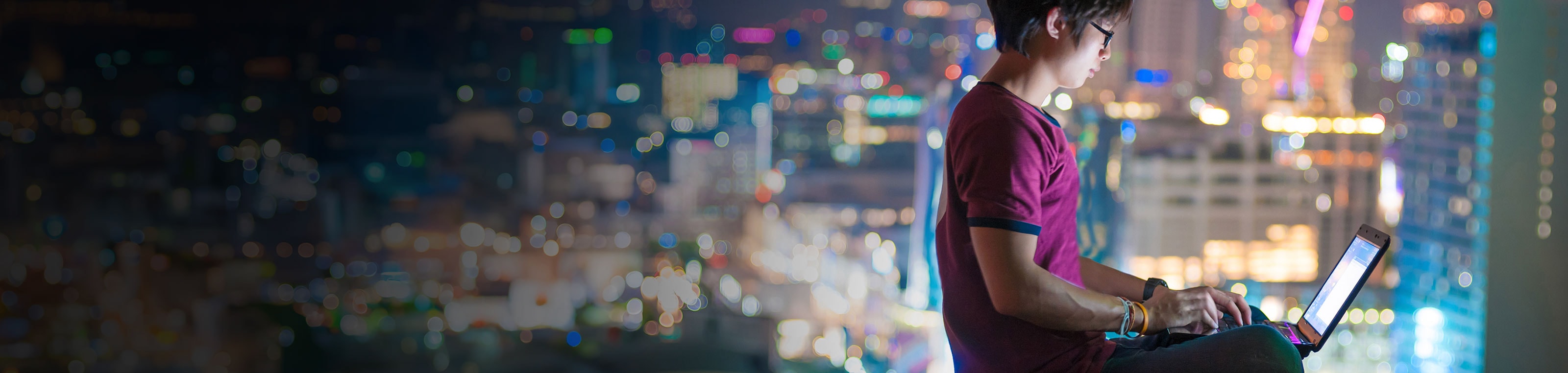 Night time city scape background with person on laptop in foreground