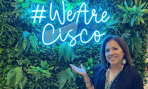 Image of a woman in front of a We Are Cisco neon sign